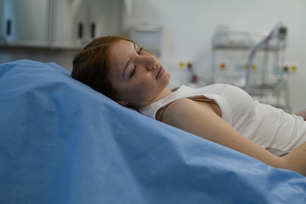Teenage girl waiting for medical examination, lying on hospital bed in tank top.