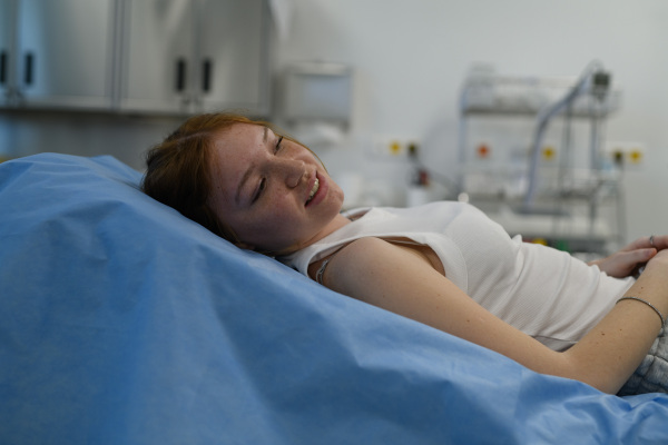 Teenage girl waiting for medical examination, lying on hospital bed in tank top.
