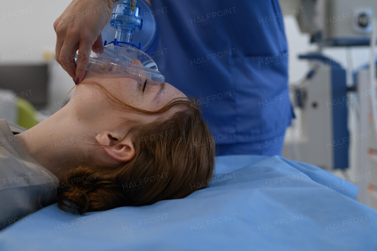 Medical staff applying oxygen mask to unconscious teenage girl in hospital. Medical procedure.