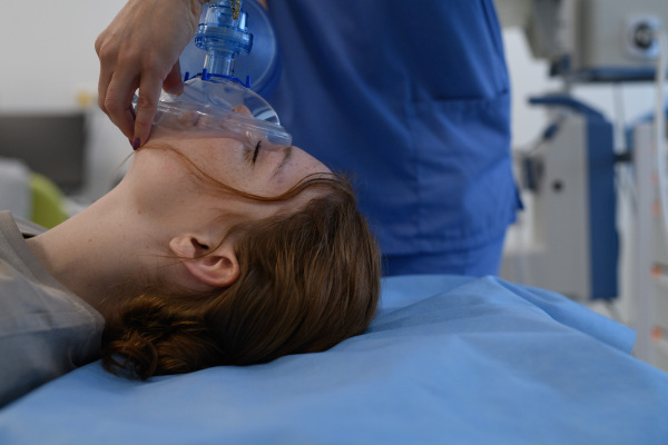 Medical staff applying oxygen mask to unconscious teenage girl in hospital. Medical procedure.