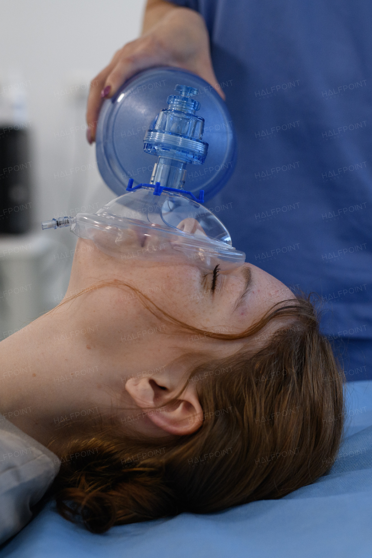 Medical staff applying oxygen mask to unconscious teenage girl in hospital. Medical procedure.