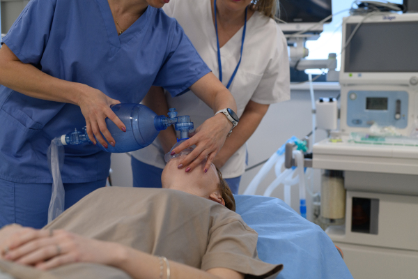 Medical staff applying oxygen mask to unconscious teenage girl in hospital. Medical procedure.