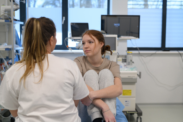 Scared teenage girl sitting on hospital bed, talking about problems with caring doctor.