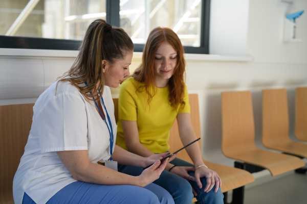 Nurse assisting adolescent patient with doctor registration paperwork in doctors office.