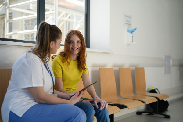 Nurse talking with teenage girl patient in modern hospital waiting room.