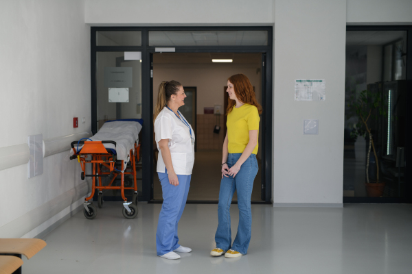 Nurse talking with teenage girl patient in modern hospital waiting room.
