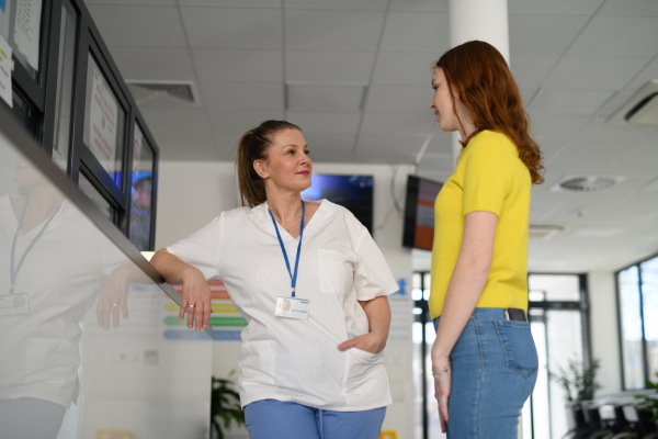 Nurse talking with teenage girl patient in modern hospital waiting room.