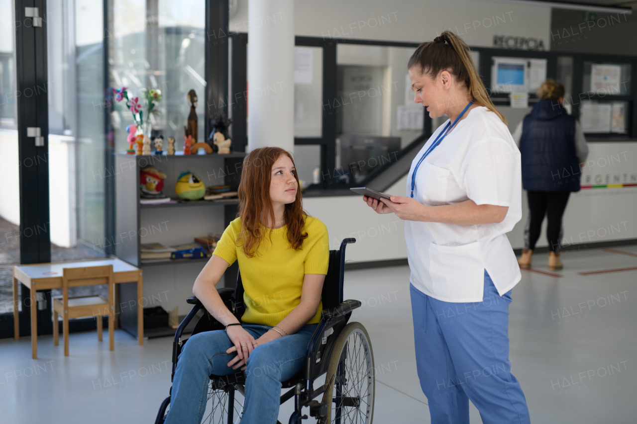 Nurse with young female patient in wheelchair at hospital, modern clinic.