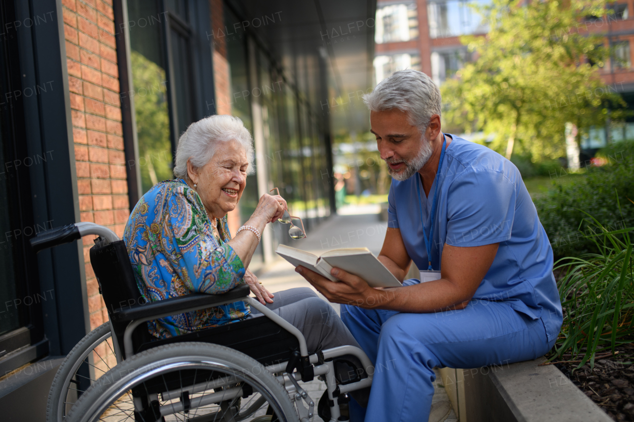 Male caregiver reading book to senior woman in a wheelchair.