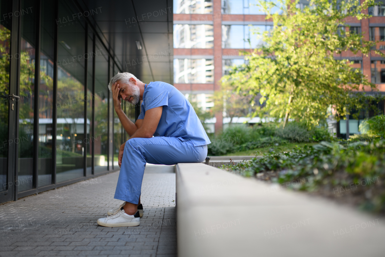 Frustrated and burnt-out doctor sitting outside the hospital, feeling down. Mental health problems.