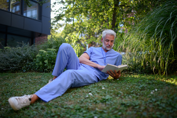 Healthcare worker resting in park outside hospital and reading book during break.