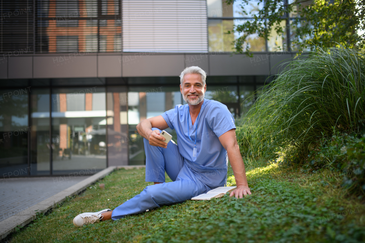 Healthcare worker resting in park outside hospital and holding smartphone.