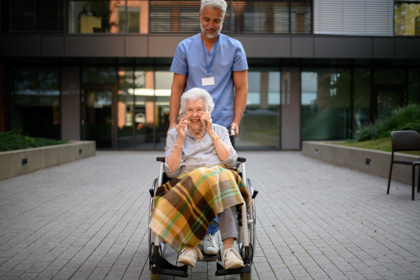 Male caregiver pushing senior woman in a wheelchair.