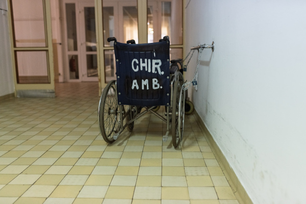 Vintage hospital wheelchair chained to wall in tiled corridor