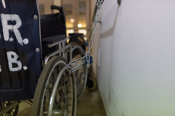 Vintage hospital wheelchair chained to wall in tiled corridor
