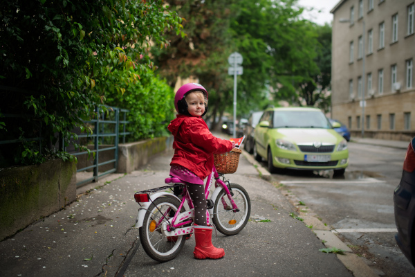 Little girl riding pink bike with basket, wearing helmet for safety.