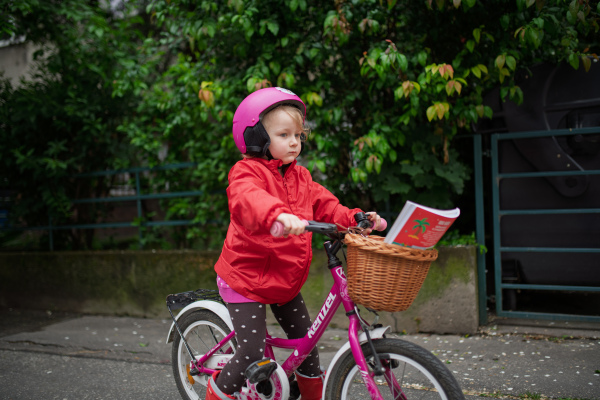 Little girl riding pink bike with basket, wearing helmet for safety.