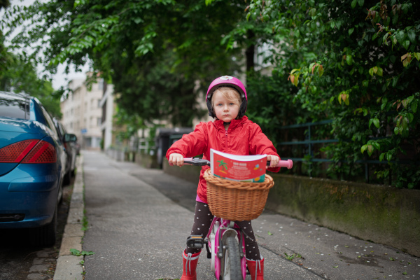 Little girl riding pink bike with basket, wearing helmet for safety.