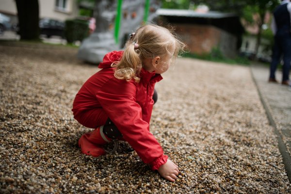 Child in red raincoat spending free time on playground in the city.