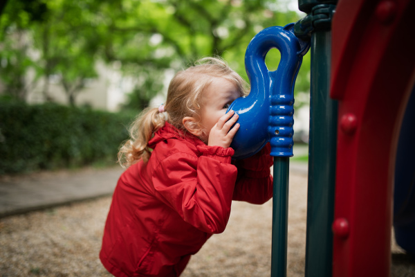 Curious girl peeking through playground tube, having fun.