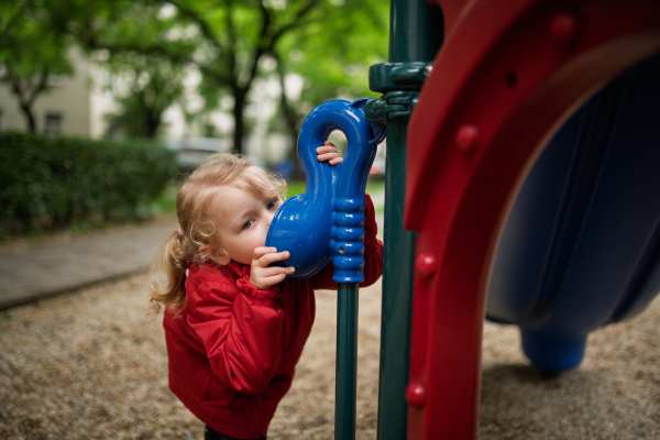 Curious girl peeking through playground tube, having fun.