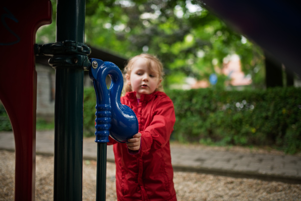 Child in red raincoat spending free time on playground in the city.