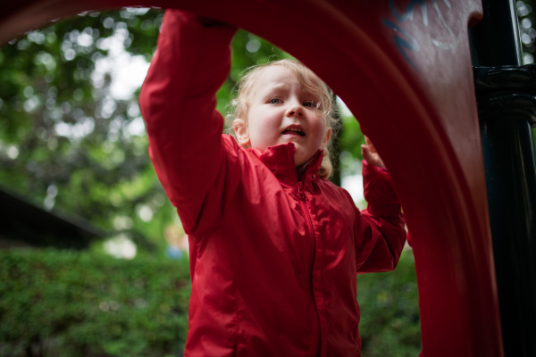 Little girl in red coat resting at play area.