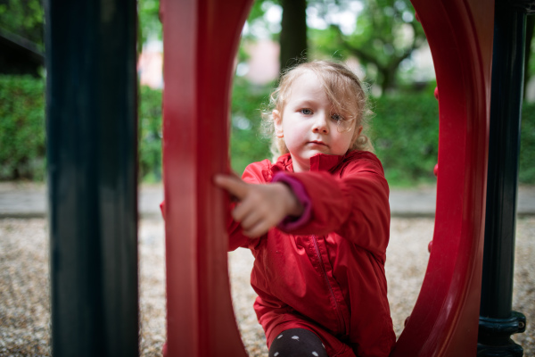 Little girl in red coat resting at play area.