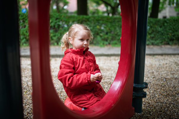 Little girl in red coat resting at play area.