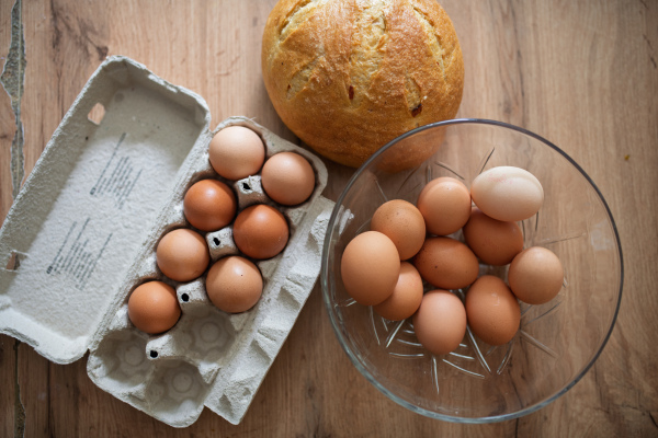 Fresh brown eggs in carton and glass bowl. Farm-fresh eggs on wooden kitchen table.