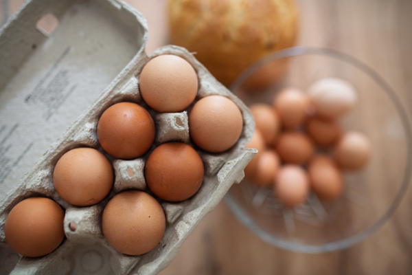 Fresh brown eggs in carton and glass bowl. Farm-fresh eggs on wooden kitchen table.