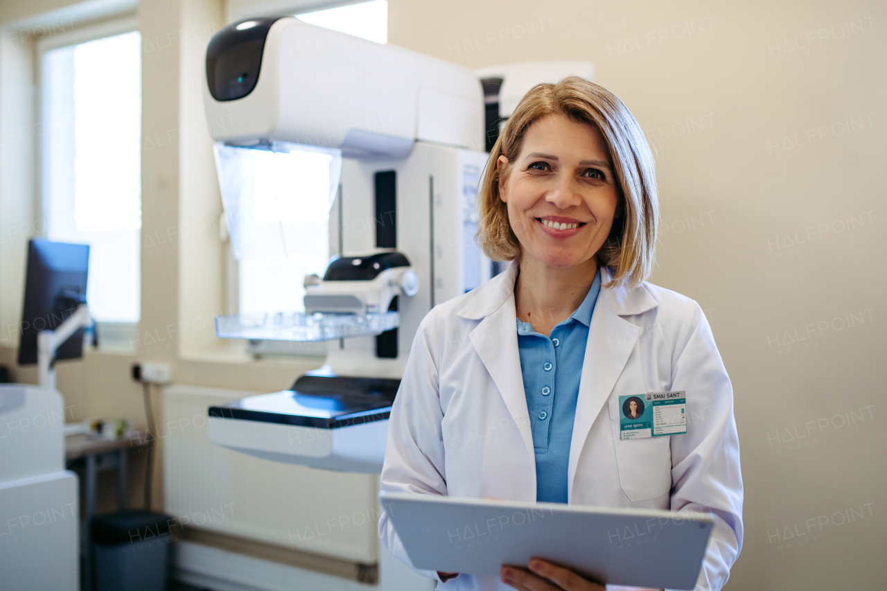 Smiling doctor standing next to mammogram machine in hospital. Preventive breast cancer screening.