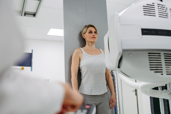 Female patient undergoing dynamic X-ray scan using tilting fluoroscopy wall unit, radiographic table with wall stand.