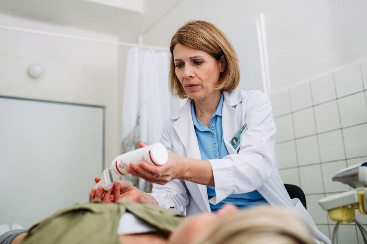 Radiologist applying gel to ultrasound probe before abdominal scan. Medical procedure.