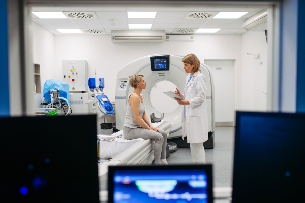 Doctor explaining CT scan results to female patient in imaging room, medical setting.