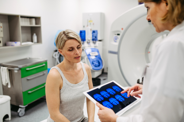 Doctor explaining CT scan results to female patient in imaging room, medical setting.