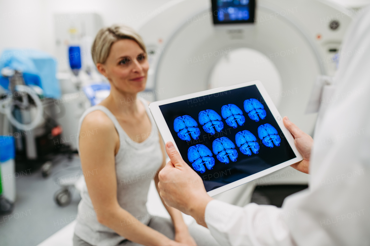 Doctor explaining CT scan results to female patient in imaging room, medical setting.