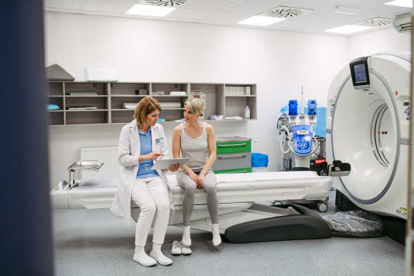 Doctor explaining results from CT scan to patient in diagnostic imaging room. Medical consultation.