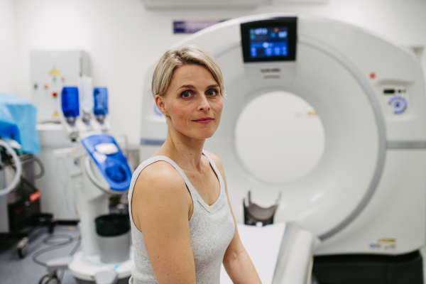 Anxious woman sitting on CT scanner bed, waiting for examination