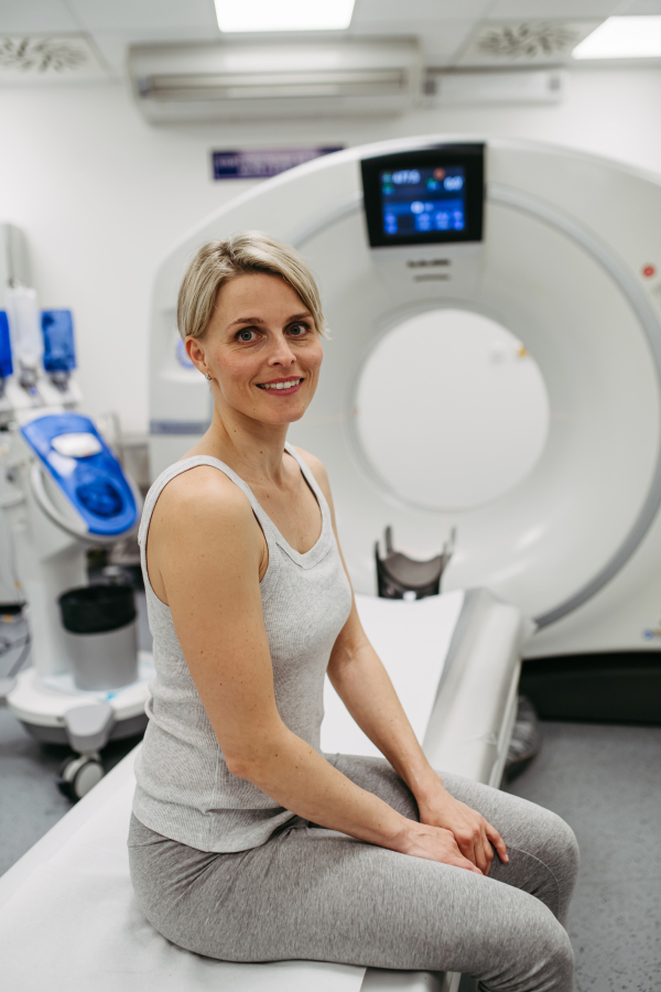 Anxious woman sitting on CT scanner bed, waiting for examination