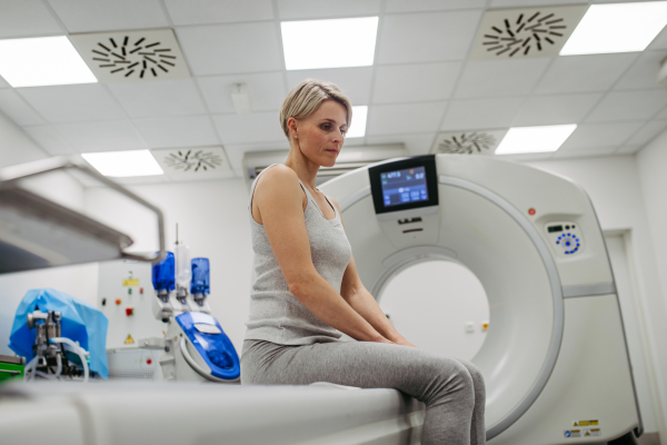 Anxious woman sitting on CT scanner bed, waiting for examination