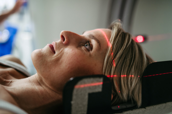 Patient positioned for head scan with laser alignment in CT scanner. Red laser lines.