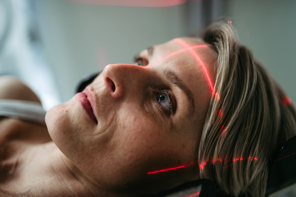Patient positioned for head scan with laser alignment in CT scanner. Red laser lines.