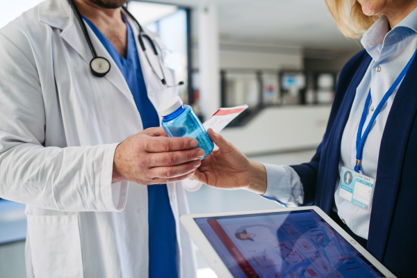 Female medical sales representative introducing pharmaceutical products to doctor. Hospital setting.