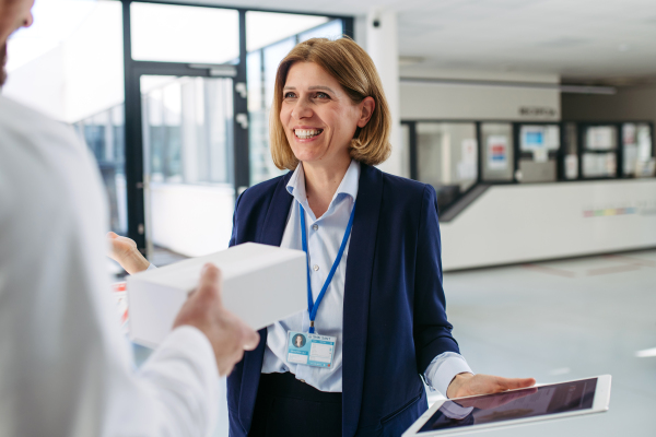 Female medical sales representative presenting medication to doctor, standing in hospital hallway.