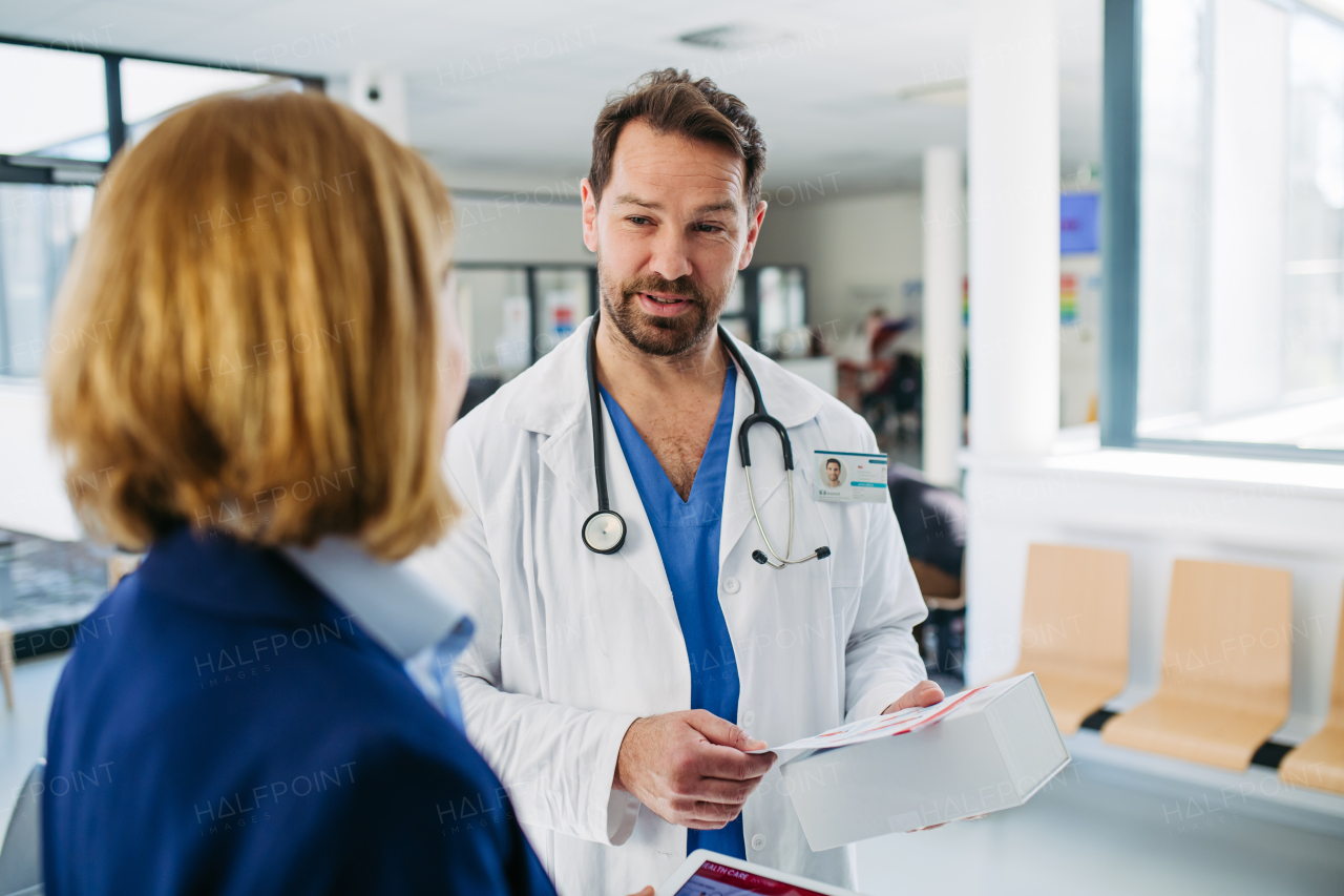 Female medical sales representative presenting medication to doctor, standing in hospital hallway.