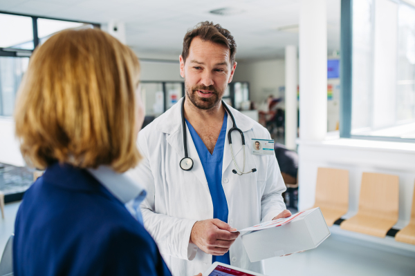 Female medical sales representative presenting medication to doctor, standing in hospital hallway.