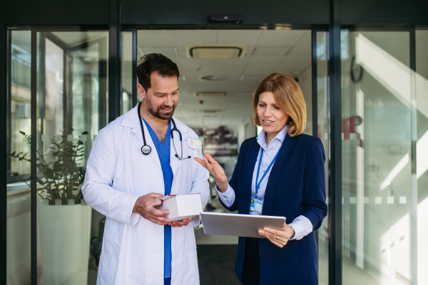 Confident female medical sales representative introducing pharmaceutical products to doctor. Hospital setting.