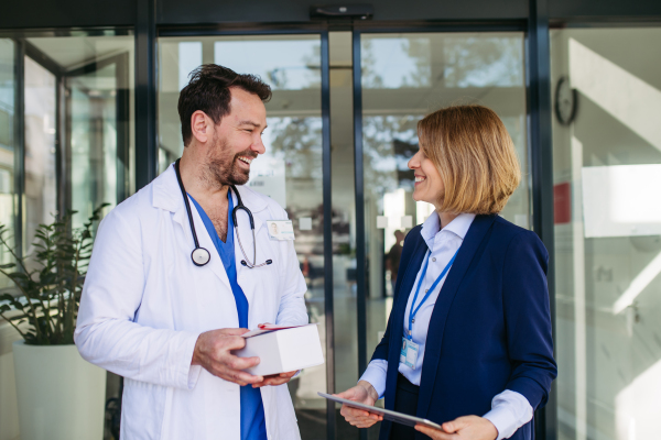 Female medical sales representative presenting medication to doctor, standing in hospital hallway.