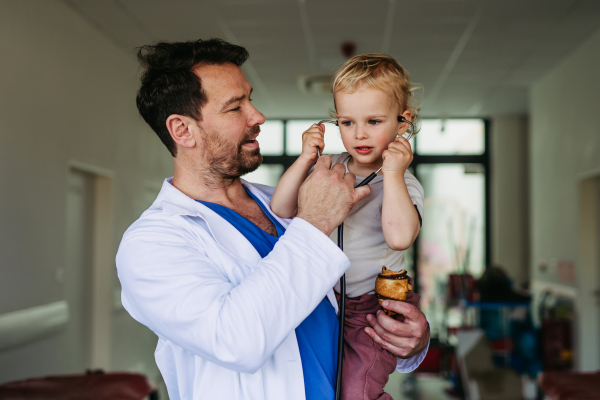 Handsome doctor holding young pediatric patient in arms. Healthcare worker as working father.